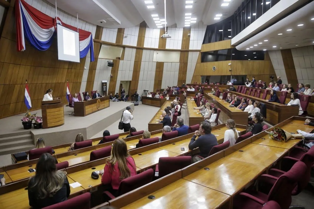 Daiana en el recinto de un parlamento, con la bandera del Paraguay